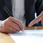 People hand pointing to sign documents.