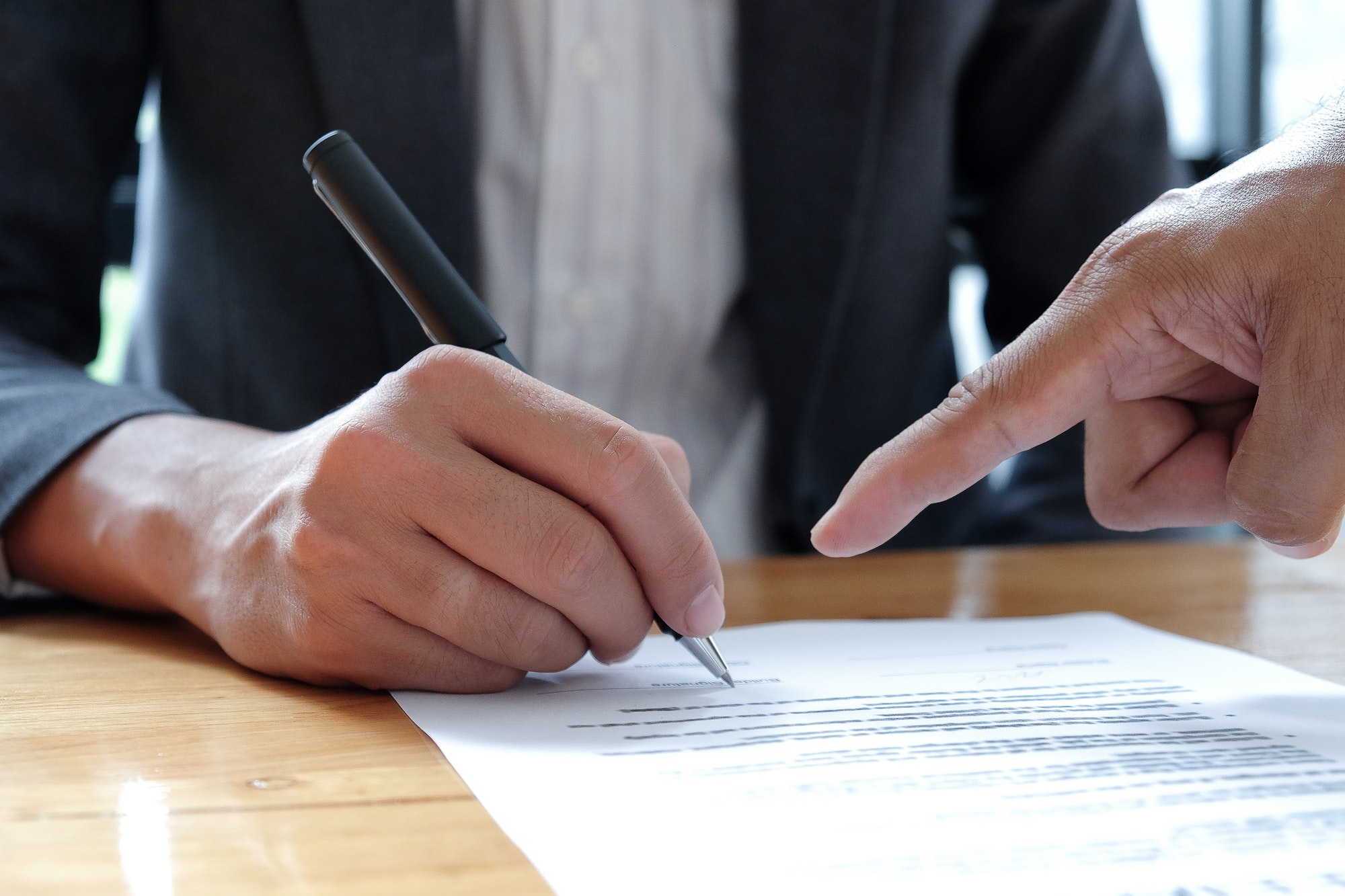 People hand pointing to sign documents.